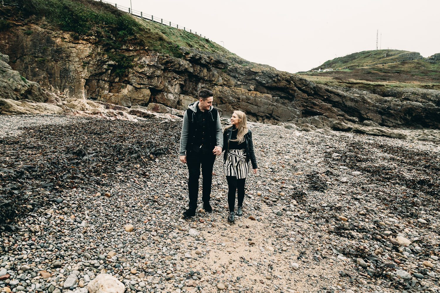 Bride and groom walk hand in hand talking on seaside engagement shoot