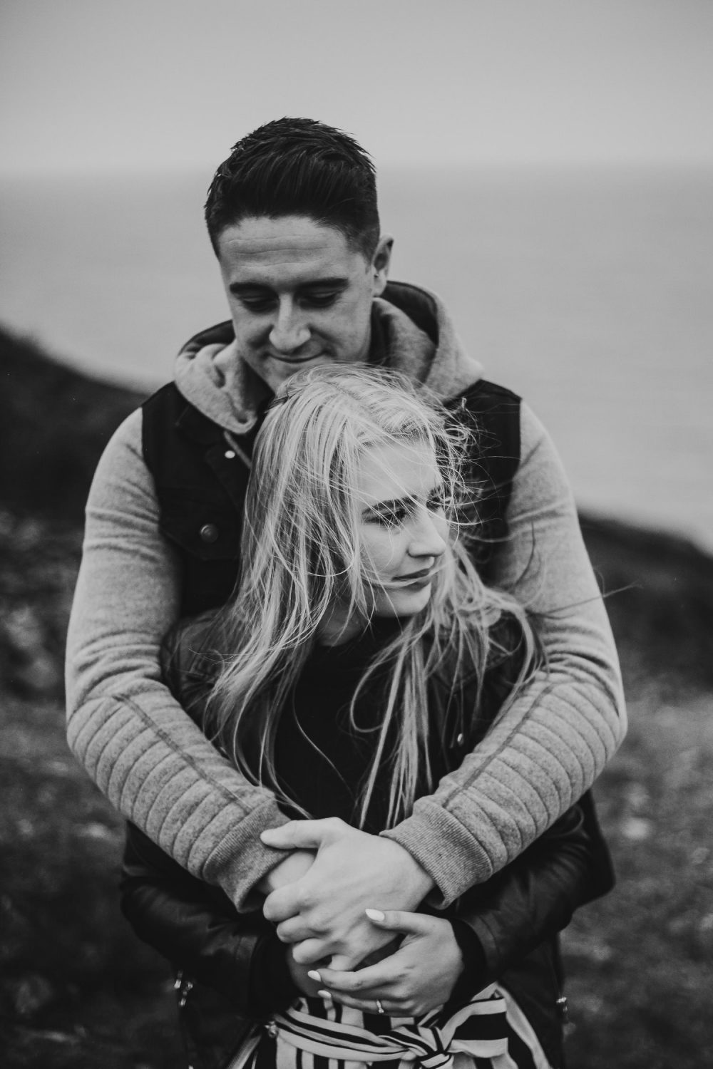 Black and white bride and groom embrace during windy engagement shoot