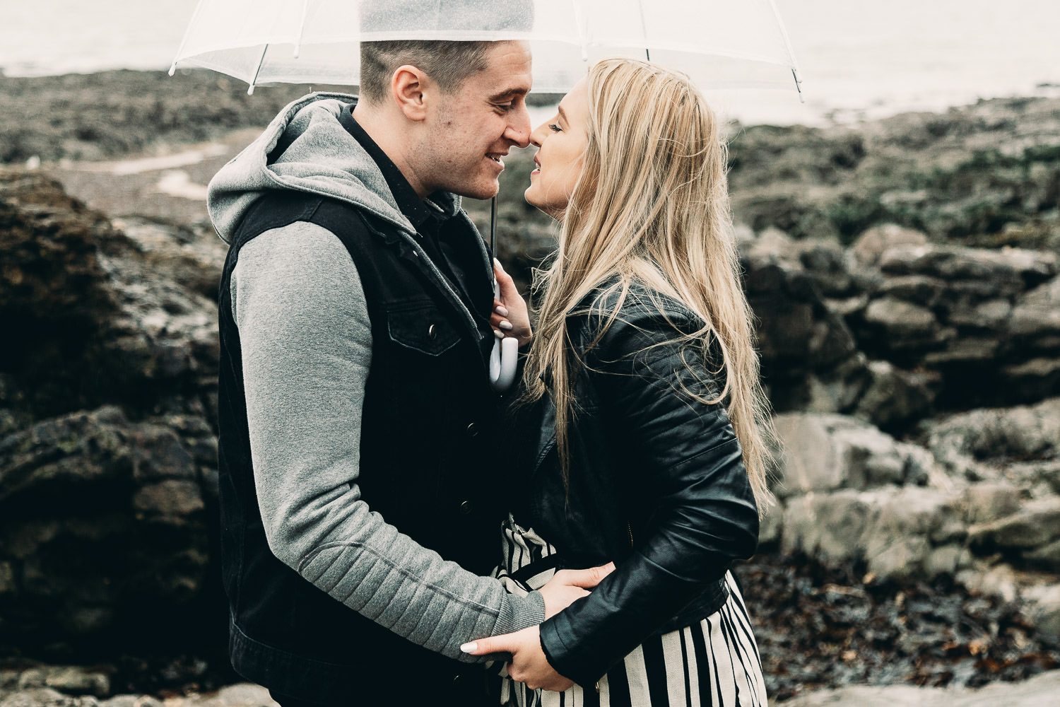 Bride and groom kiss under umbrella on seaside engagement shoot