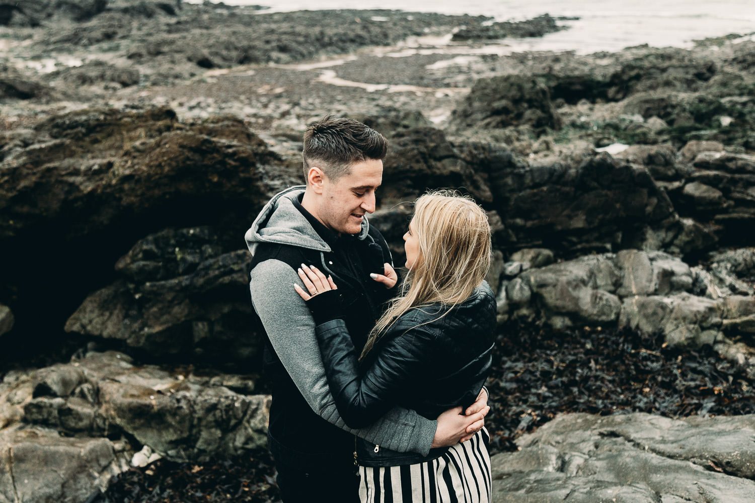 Bride and groom embrace on windy seaside engagement shoot