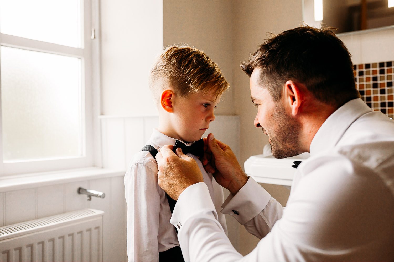 groom in black tuxe helping son with wedding suit