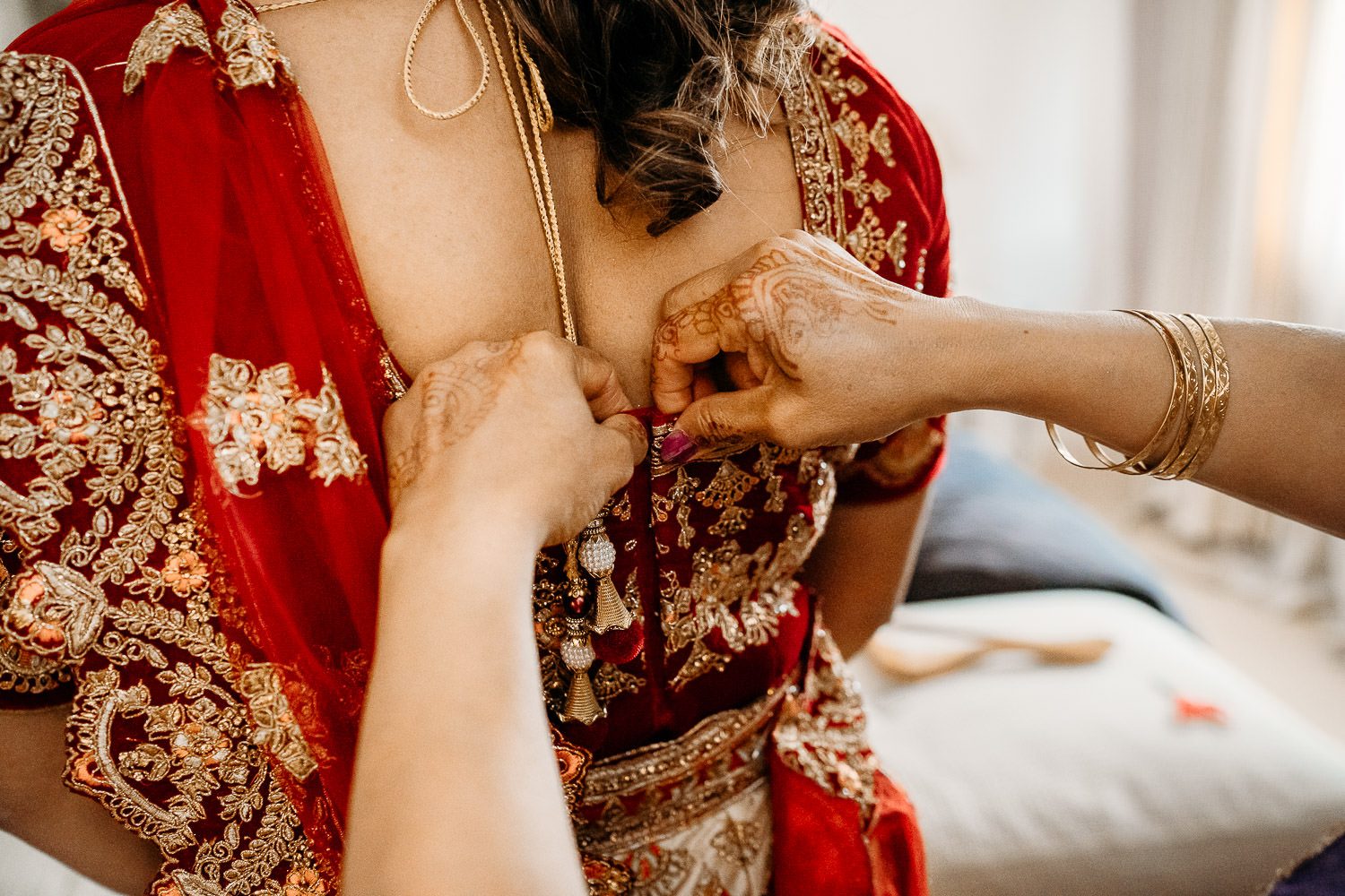 brides mother helping bride put on red sari for wedding