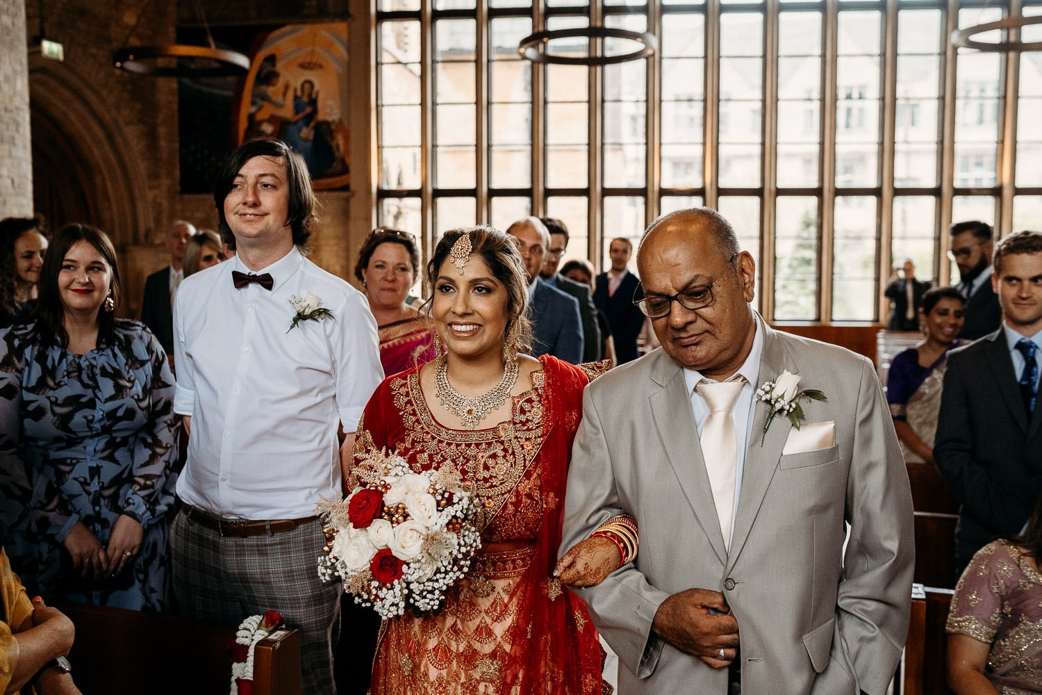 bride in red sari walking down isle with father at uppingham chapel