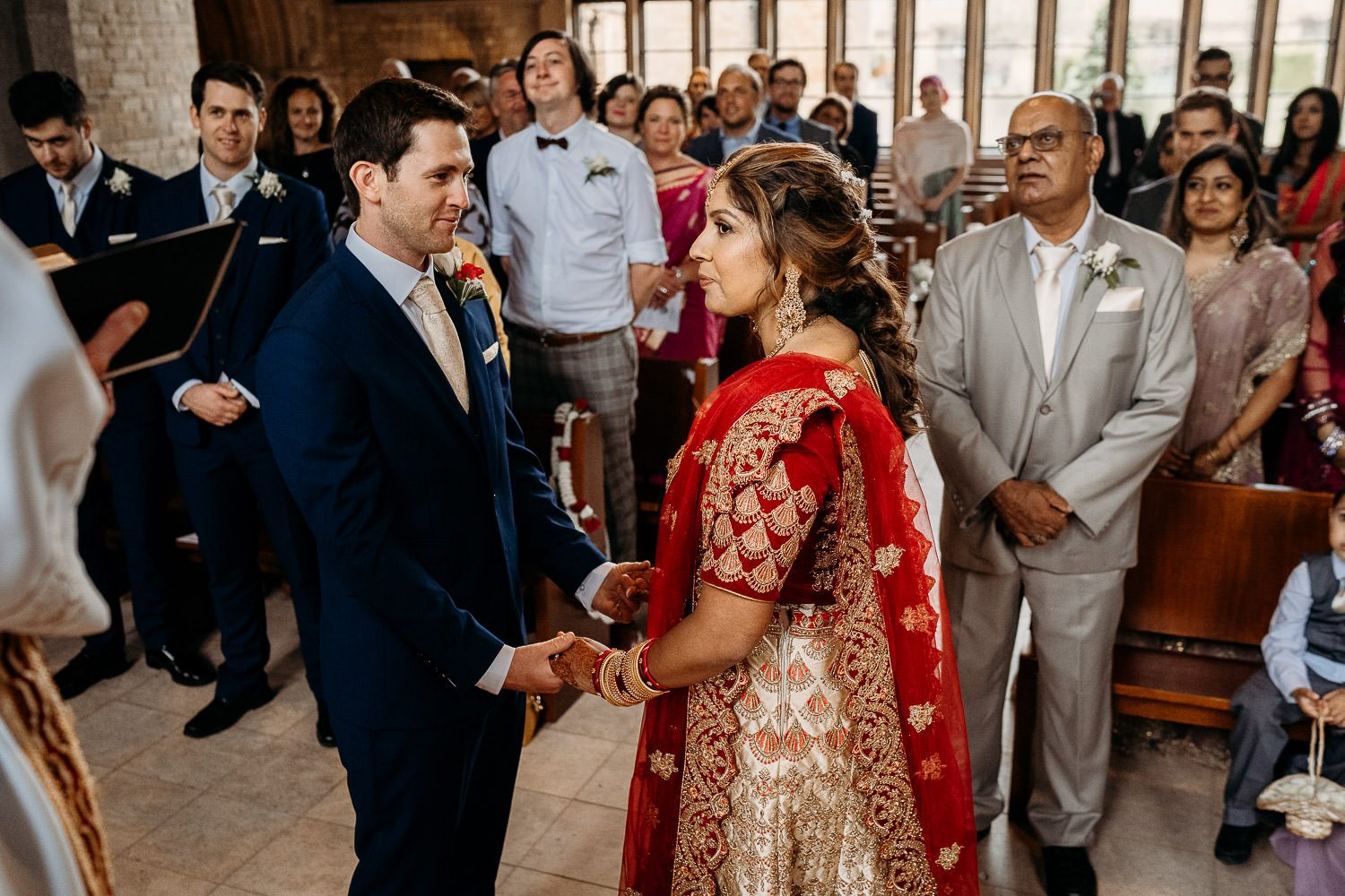 groom smiling at bride in red sari during wedding ceremony