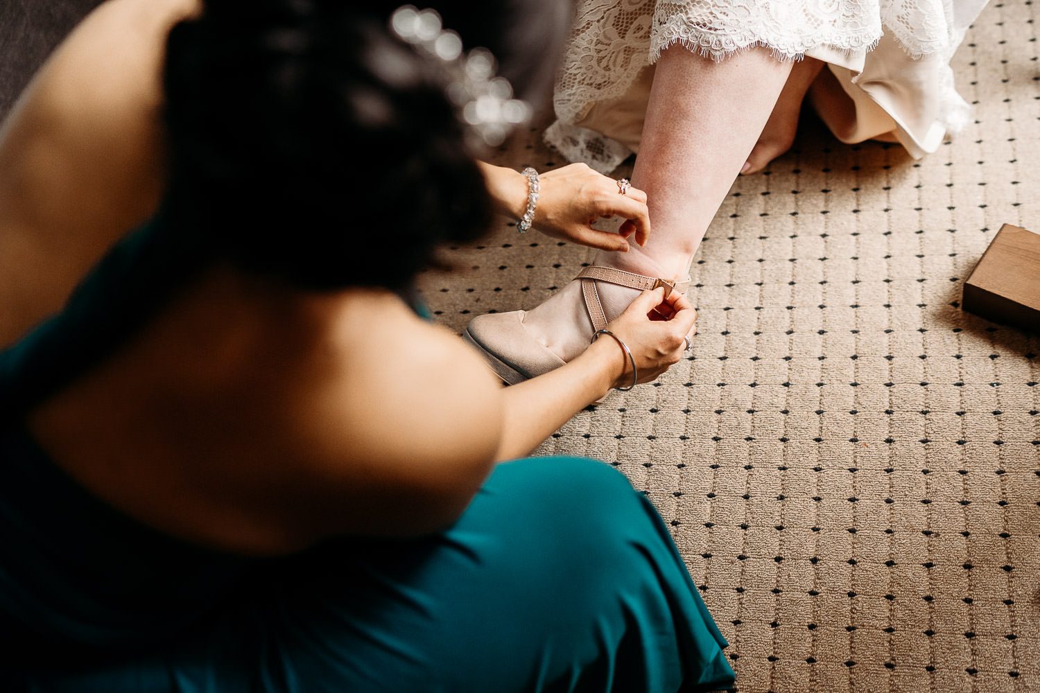 bridesmaid helping bride put on nude wedding shoes