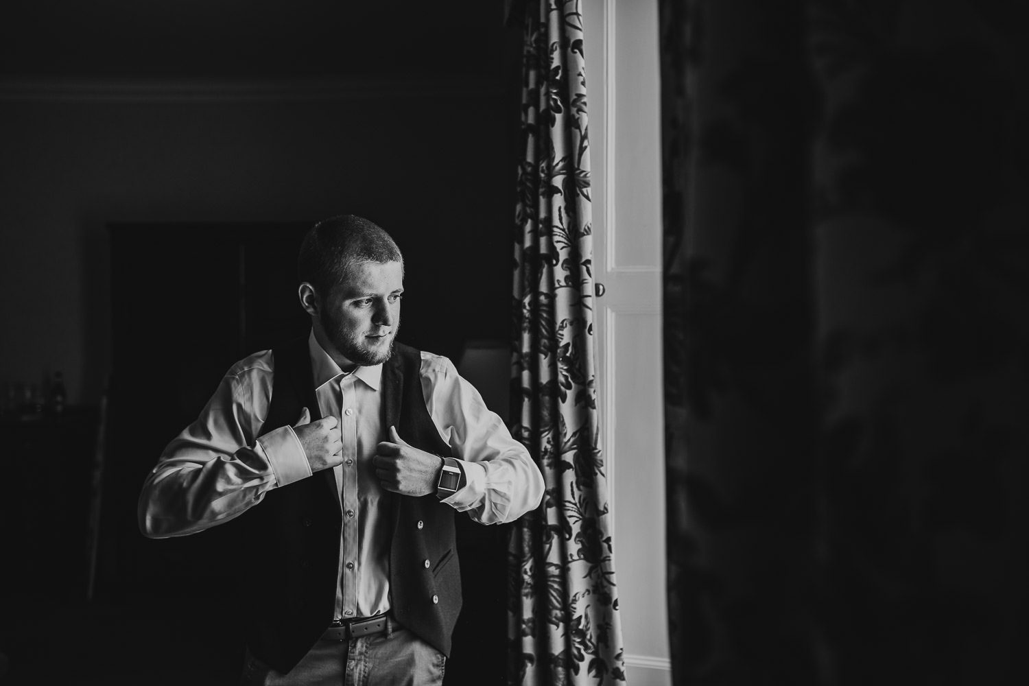 groom putting on waistcoat in mercure elcot hotel bridal suite