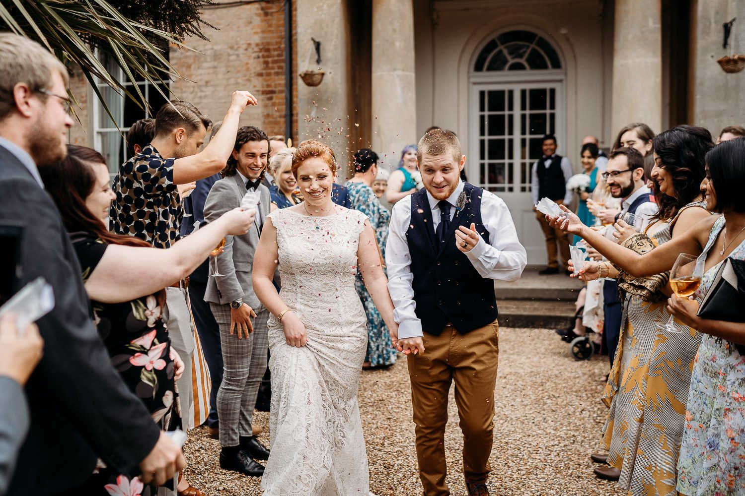 quirky bride and groom having colourful real petal confetti thrown at them