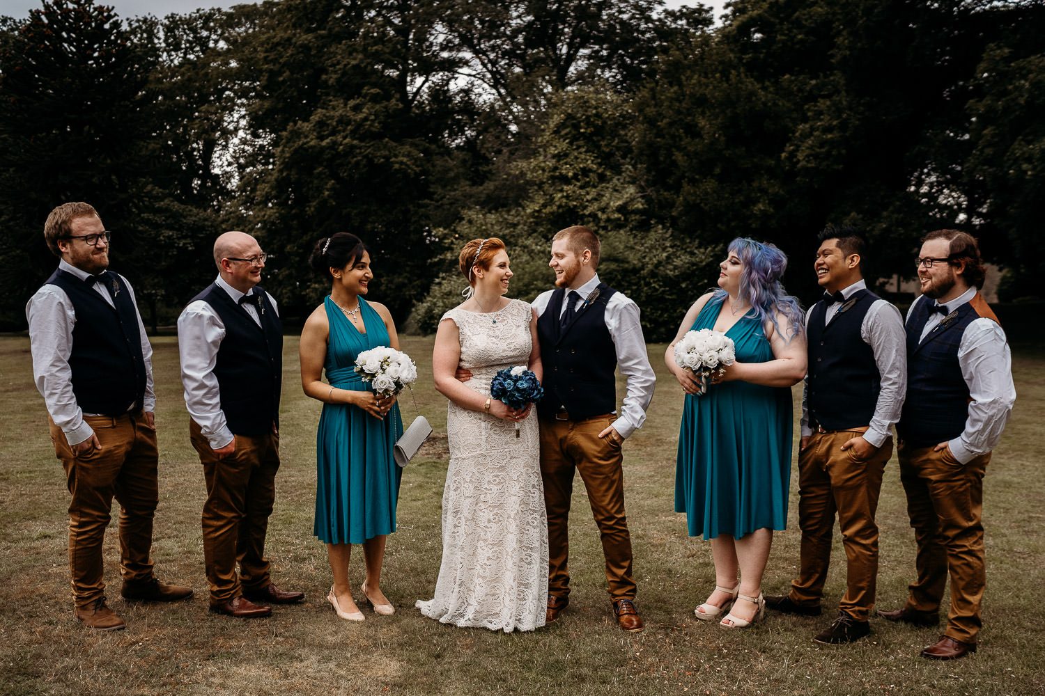 bridesmaids and groomsmen all looking at bride and groom and smiling during family portraits