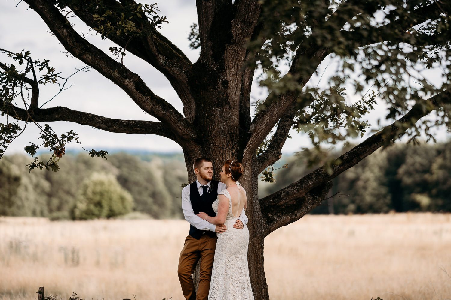 romantic groom leaning on tree and holding bride