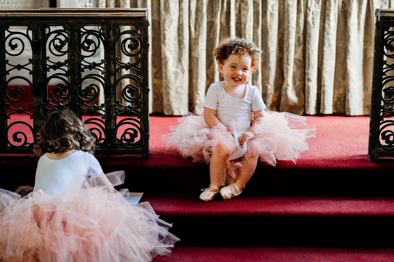 young flower girl in pink tulle skirt sitting on church steps